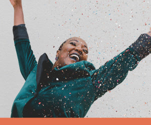Image of woman in teal coat rejoicing, surrounded by confetti
