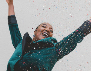 Image of woman in teal coat rejoicing, surrounded by confetti