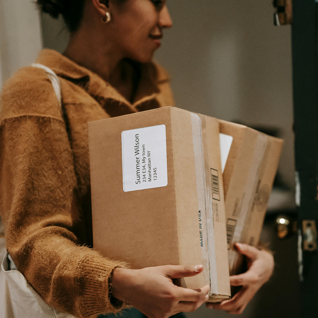 Person holding a cardboard box with a label, standing in front of a door.