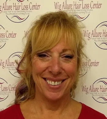 Woman named Nancy with blonde hair smiling in front of a Wig Allure Hair Loss Center backdrop